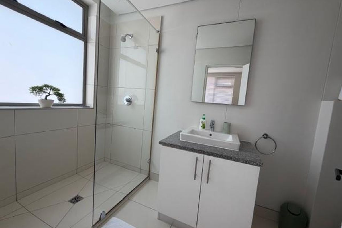 Modern bathroom featuring a glass-enclosed walk-in shower, vanity cabinet with a countertop basin, and neutral tiled finishes throughout.