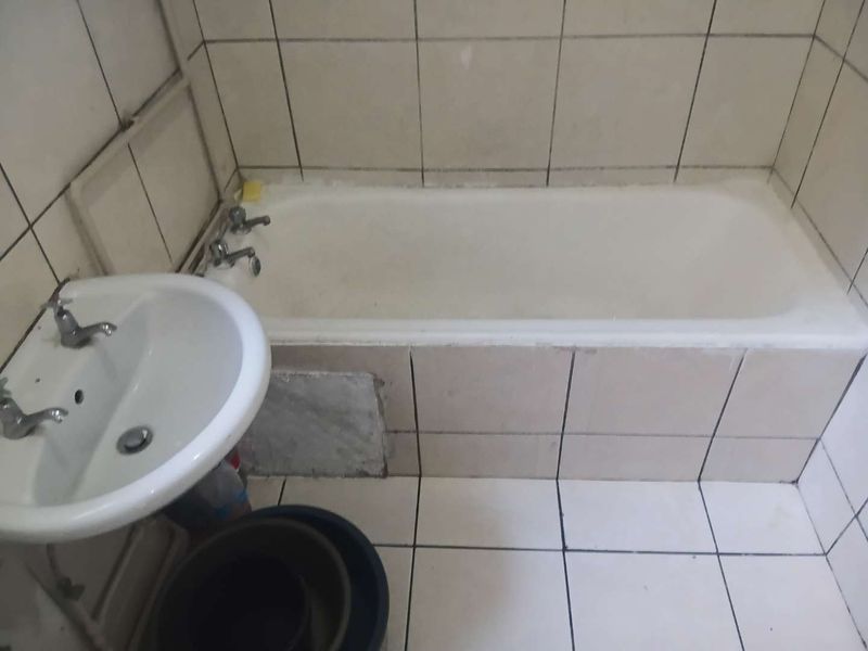A dated bathroom featuring a standard bathtub and pedestal basin with ceramic tiling throughout, requiring cosmetic updates to improve its overall condition.