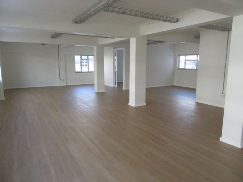 A spacious, open-plan commercial or office area featuring neutral finishes, structural columns, and exposed ceiling cable trays, offering a versatile blank canvas.