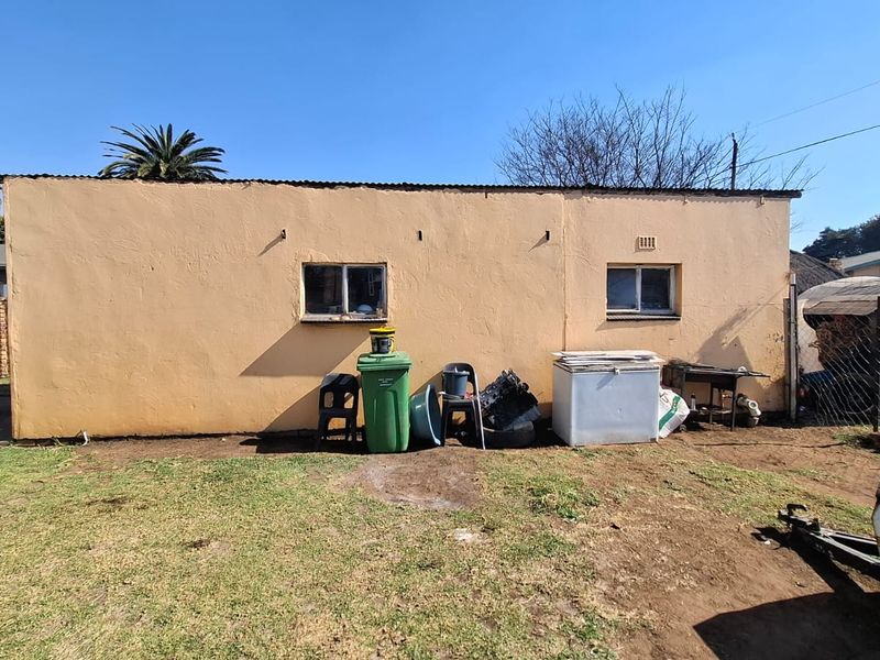 Rear exterior view of the property featuring plastered masonry walls, corrugated metal roofing, and sliding windows set against a garden area.