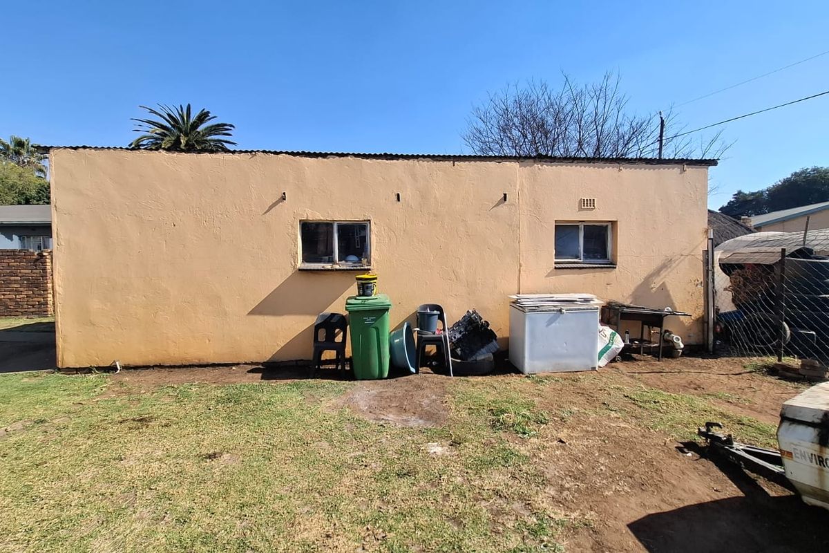 Rear exterior view of the property featuring plastered masonry walls, corrugated metal roofing, and sliding windows set against a garden area.