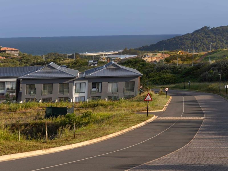 A street view showing the approach to the apartment complex with surrounding coastal landscape and ocean views.