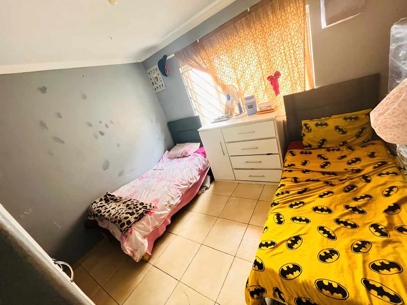 A bedroom featuring tiled flooring and security bars on the window, currently showing signs of wear on the wall surfaces.