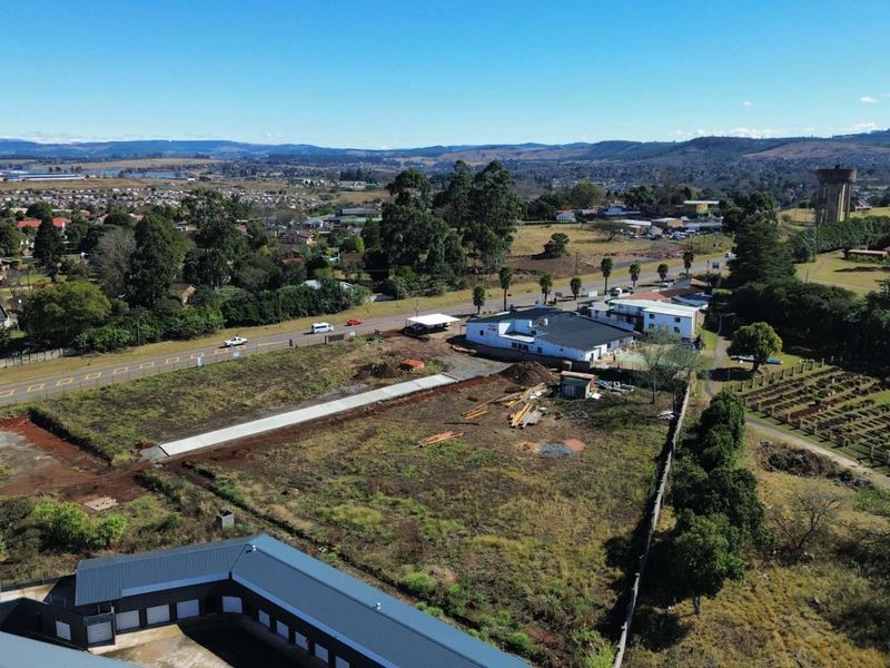 Aerial view of a commercial vacant land plot featuring existing building structures, boundary walls, and access to the main road.