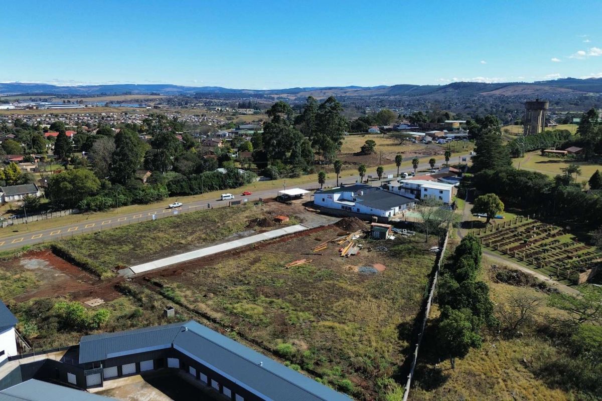Aerial view of a commercial vacant land plot featuring existing building structures, boundary walls, and access to the main road.