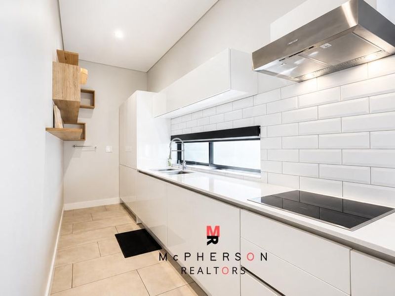 Modern galley-style kitchen featuring sleek white cabinetry, stone countertops, subway tile backsplash, and integrated stainless steel appliances.
