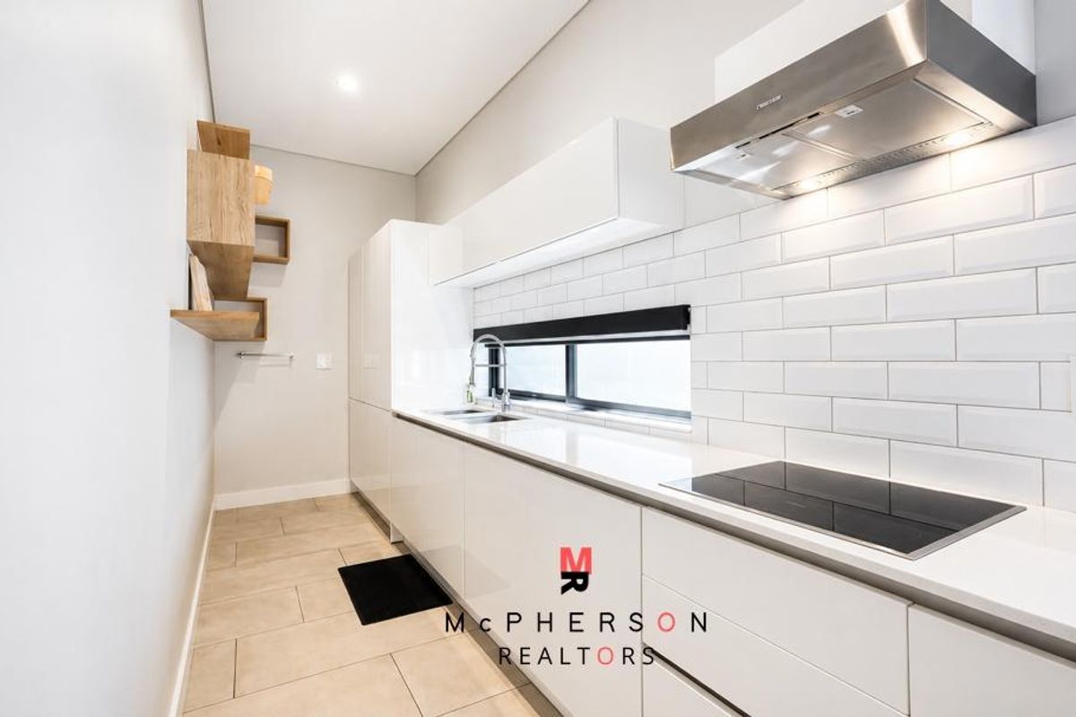Modern galley-style kitchen featuring sleek white cabinetry, stone countertops, subway tile backsplash, and integrated stainless steel appliances.