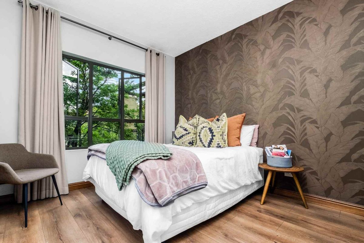 A well-maintained bedroom featuring wood-look flooring, a large window with natural light, and a decorative feature wall.