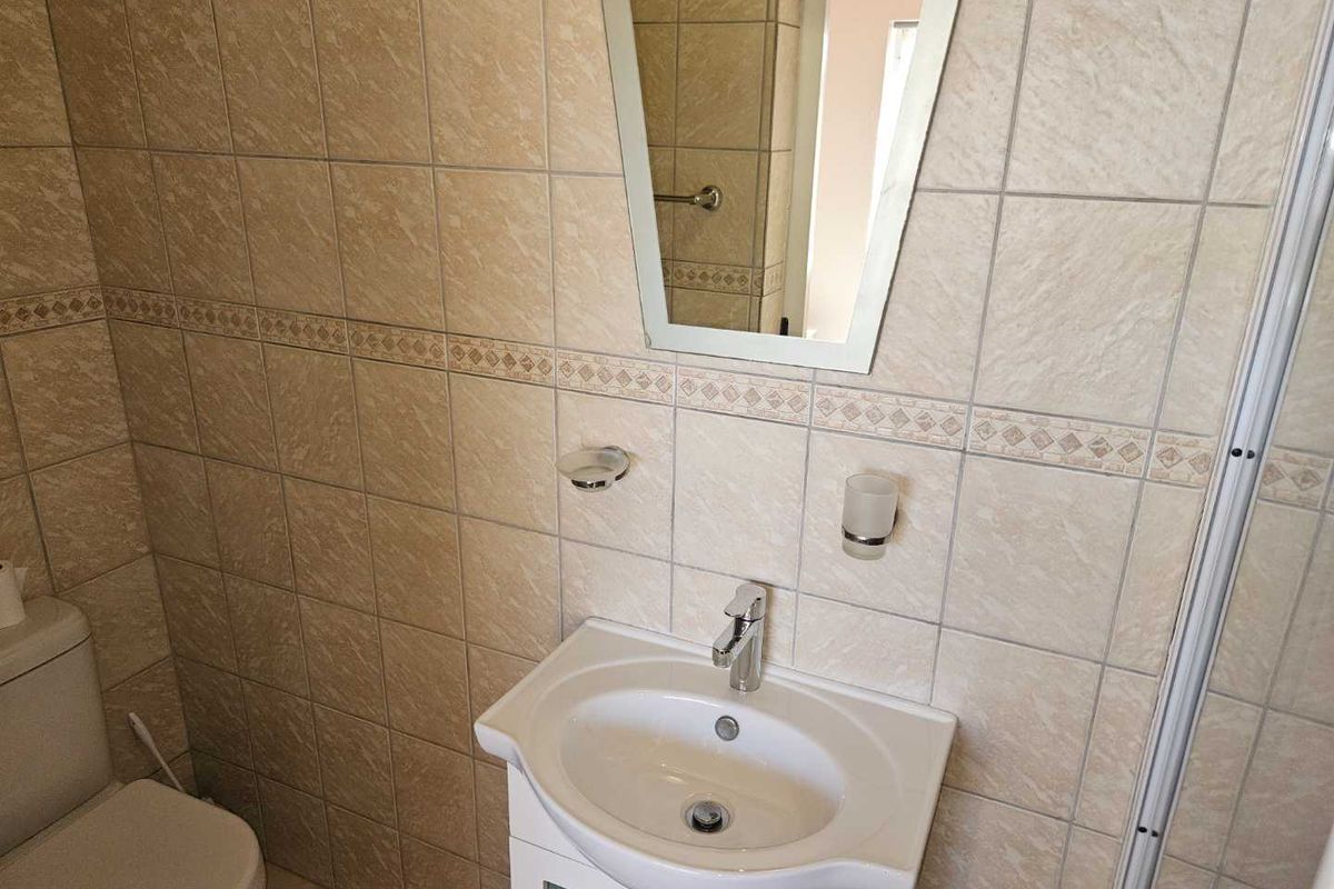 A functional bathroom featuring a vanity basin, wall-mounted mirror, and tiled walls.
