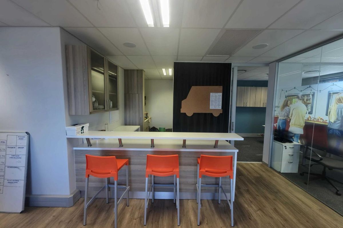 A modern office kitchenette area featuring built-in cabinetry, a breakfast bar counter, and integrated lighting within a professional workspace environment.