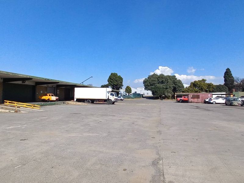 Expansive industrial yard featuring a large asphalt loading area with covered loading docks and ample space for vehicle maneuvering and storage.