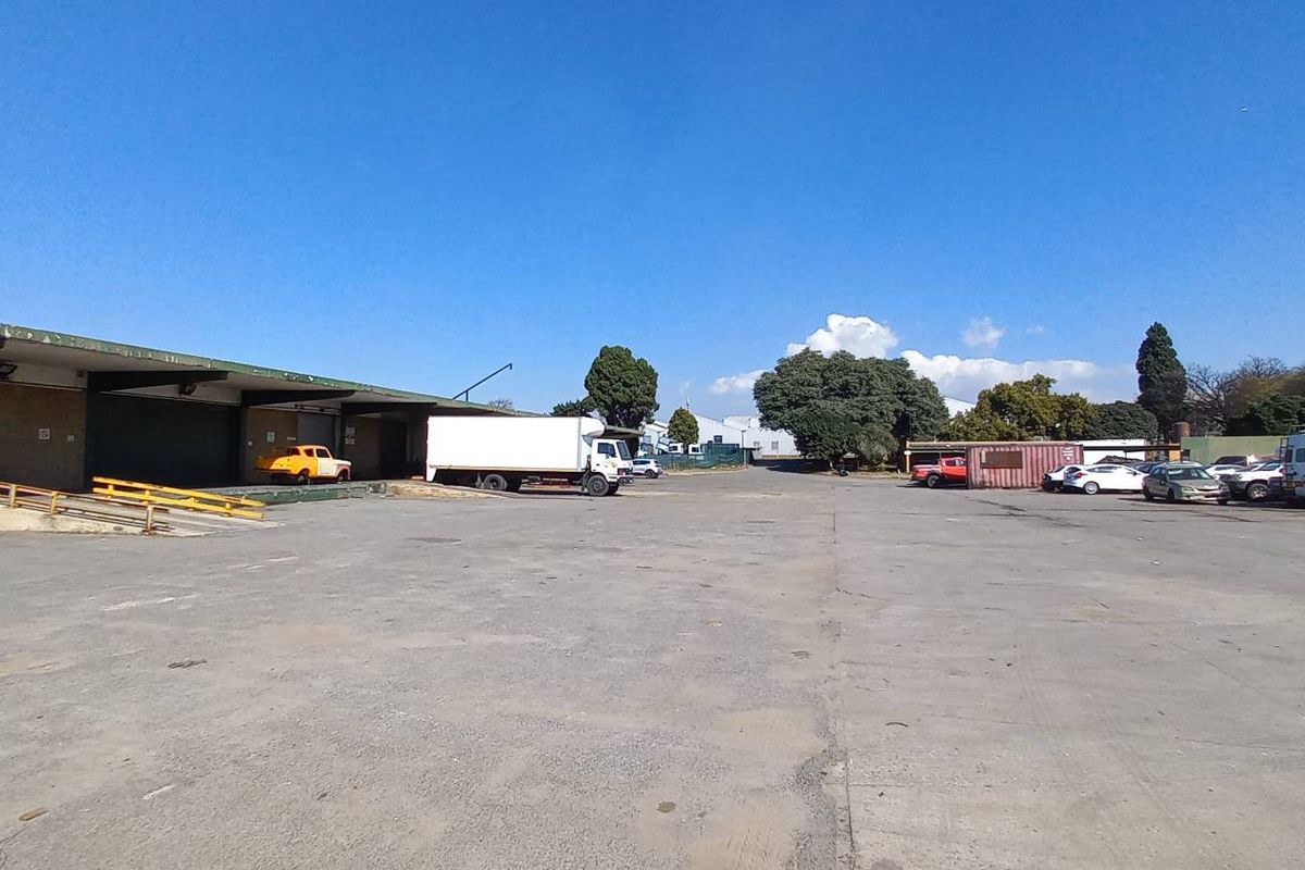 Expansive industrial yard featuring a large asphalt loading area with covered loading docks and ample space for vehicle maneuvering and storage.