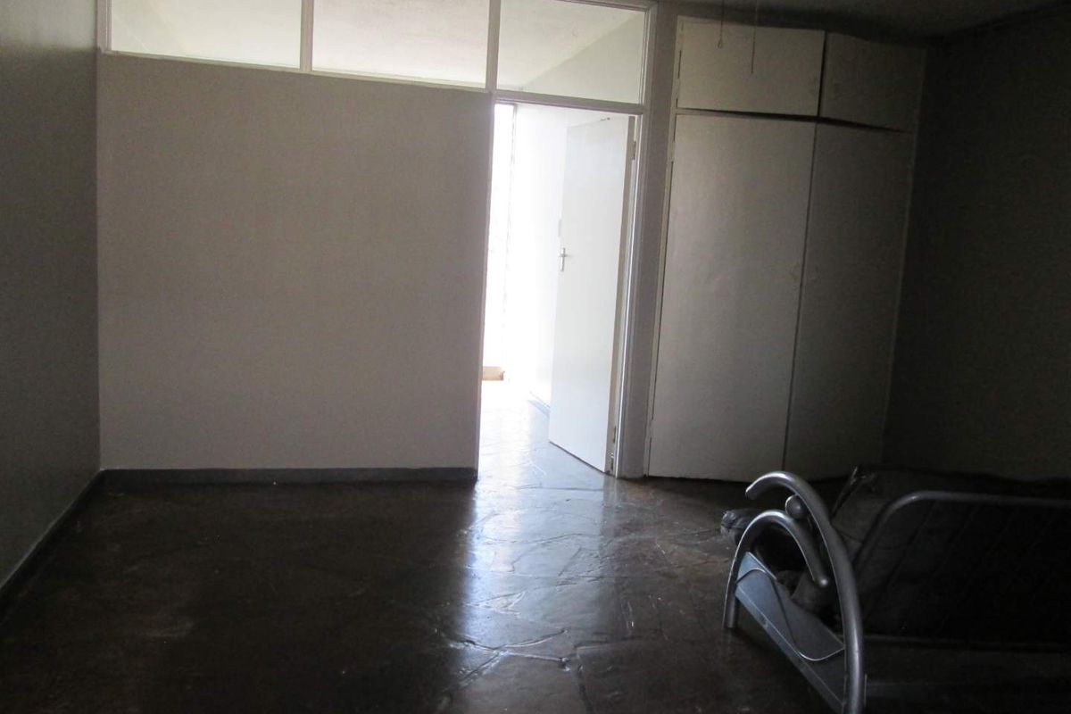 A vacant bedroom featuring built-in cupboards, tiled flooring, and a transom window above the doorway, offering a blank canvas for renovation.
