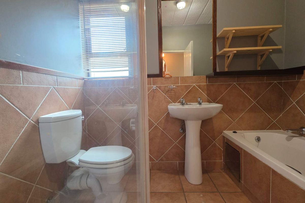 A functional bathroom featuring a pedestal sink, a bathtub, a toilet, and tiled walls with a window for natural light.