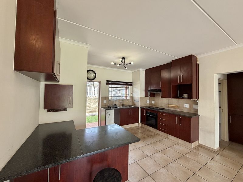 A functional kitchen featuring dark wood cabinetry, granite countertops, built-in oven and hob, and tiled flooring with direct access to the rear exterior.