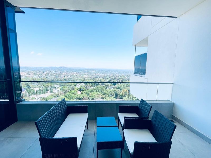 A modern covered balcony featuring a sleek glass balustrade and expansive elevated views over the surrounding landscape.