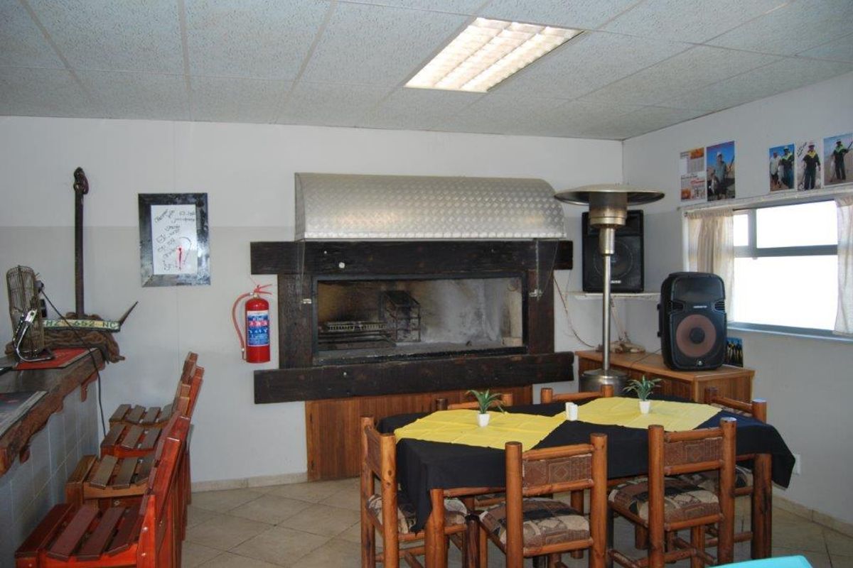 Indoor entertainment area featuring a large built-in braai with stainless steel extractor hood, tiled flooring, and drop ceiling lighting.