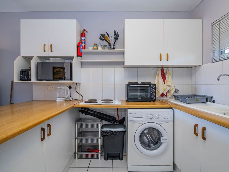 A functional kitchen featuring white cabinetry, laminate countertops, a tiled backsplash, and integrated laundry plumbing, offering a practical layout for daily use.
