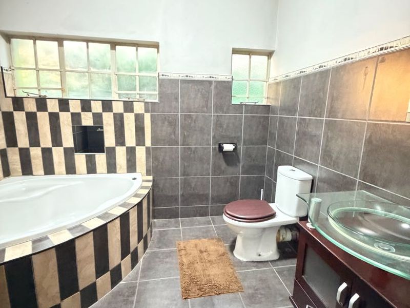 A bathroom featuring a corner bathtub with decorative tiling, a vanity unit with a glass vessel sink, and a standard toilet.