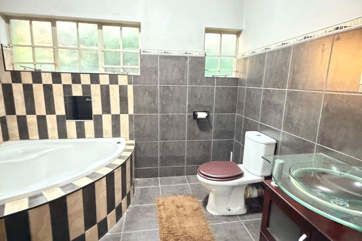 A bathroom featuring a corner bathtub with decorative tiling, a vanity unit with a glass vessel sink, and a standard toilet.