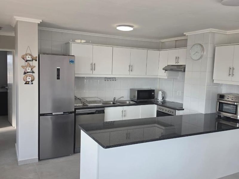 A functional kitchen featuring white cabinetry, granite countertops, a kitchen island, and a tiled backsplash, providing a clean and practical cooking space.