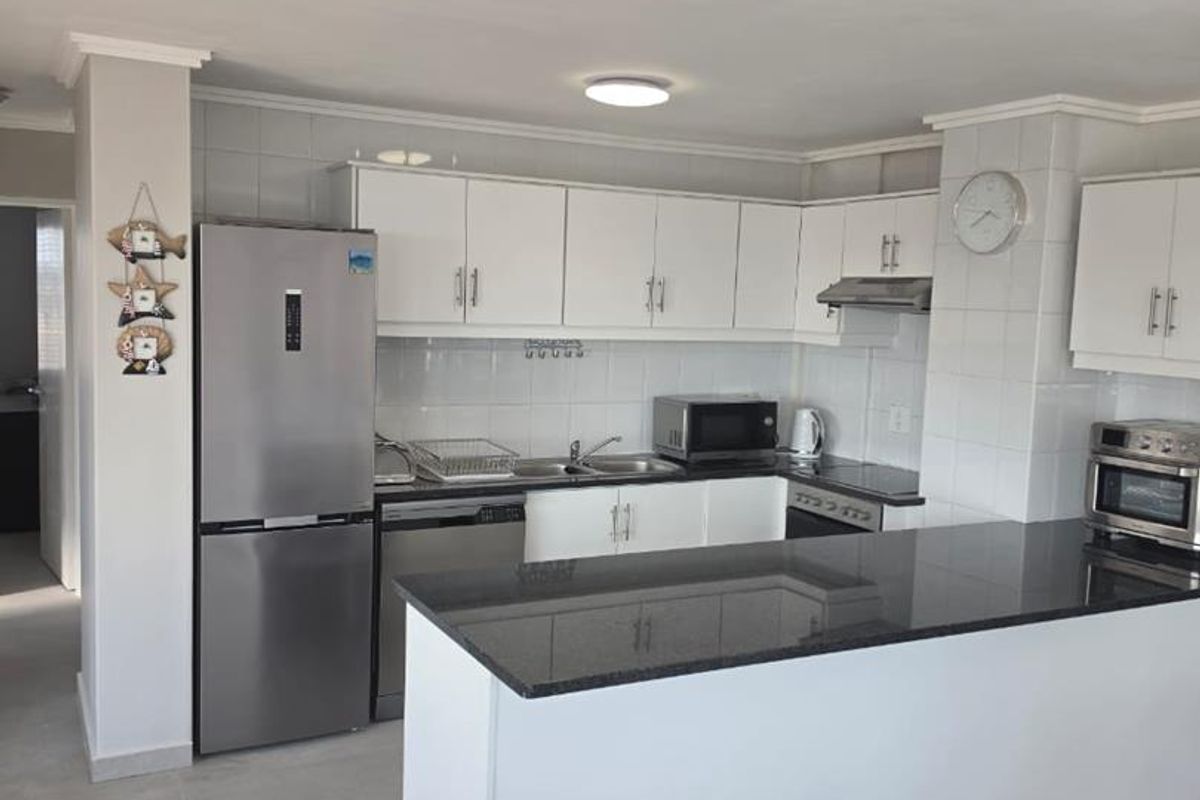 A functional kitchen featuring white cabinetry, granite countertops, a kitchen island, and a tiled backsplash, providing a clean and practical cooking space.