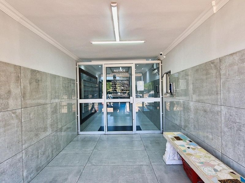 A clean and modern apartment building entrance lobby featuring large format grey wall and floor tiles, glass security doors, and integrated mailboxes.