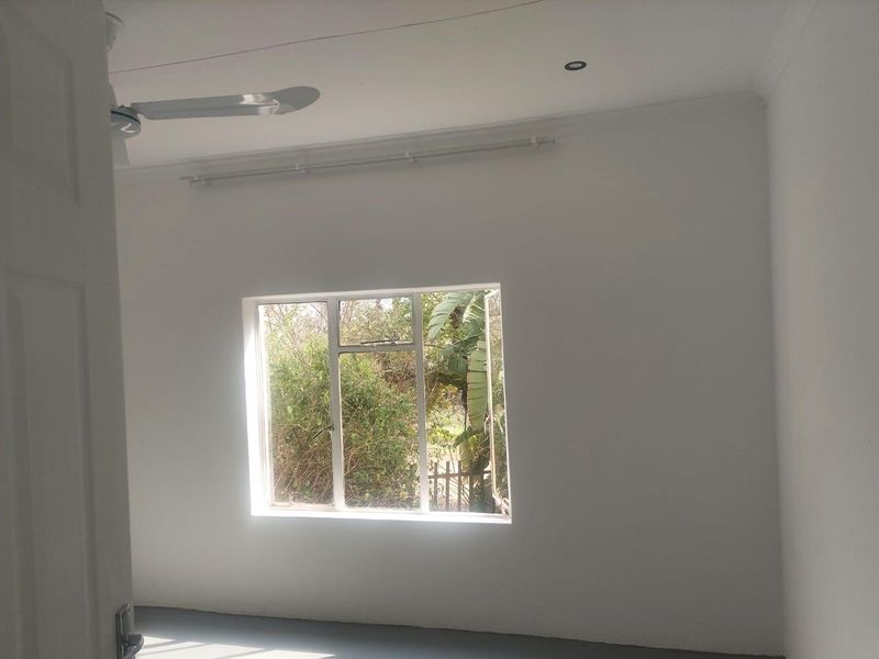 A bright, empty bedroom featuring a ceiling fan, recessed lighting, and a window overlooking the garden.
