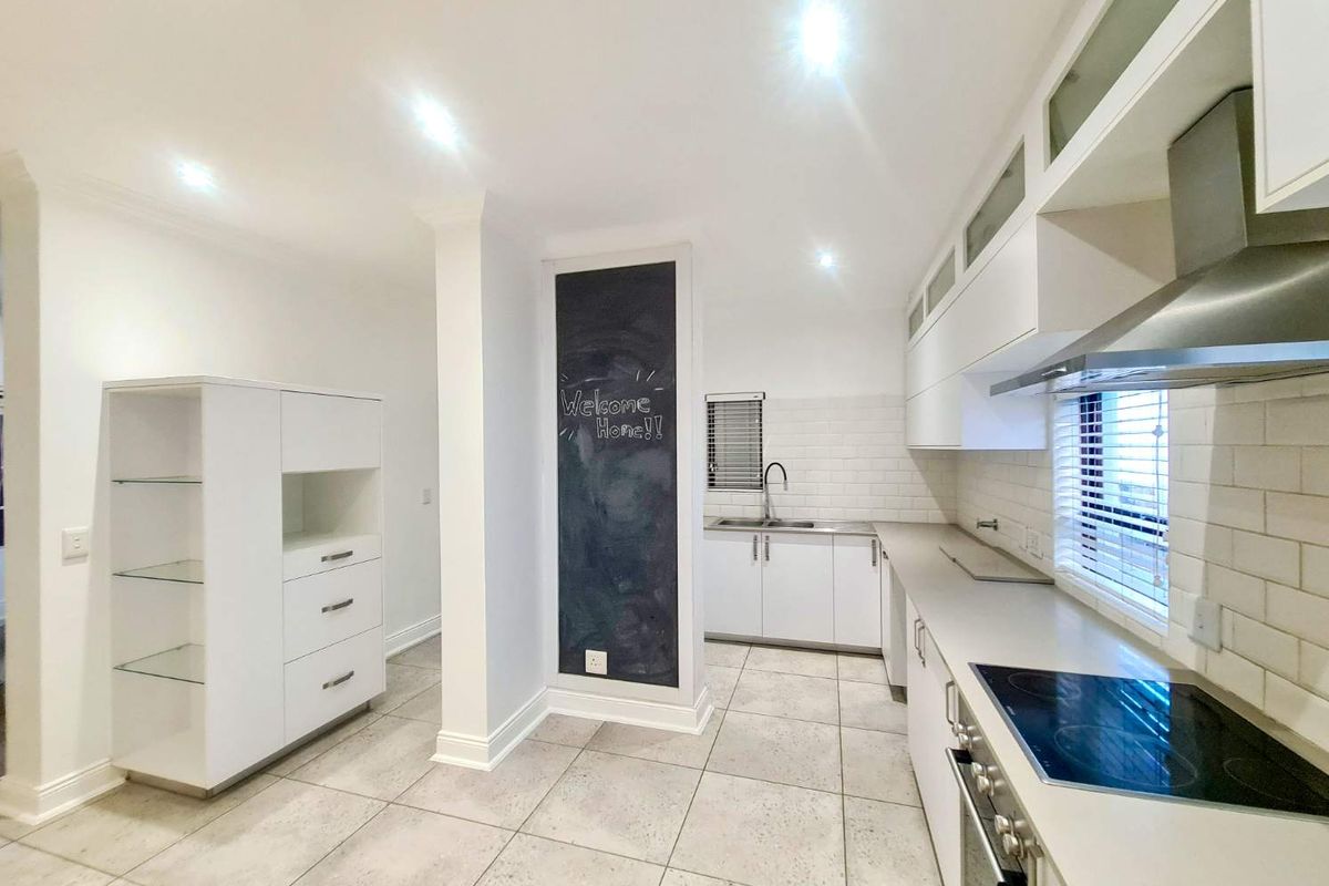 Modern kitchen featuring white cabinetry, subway tile backsplash, integrated oven, electric cooktop, stainless steel extractor fan, and tiled flooring.
