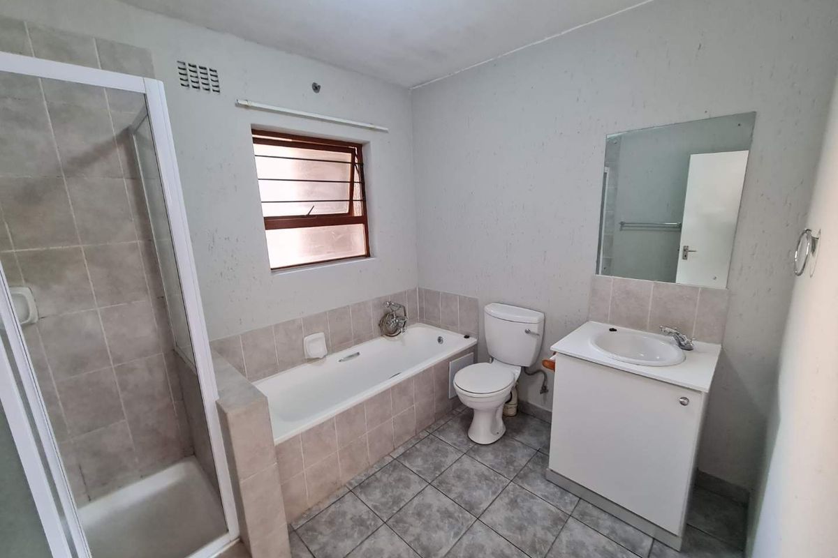 A functional bathroom featuring a separate shower enclosure, bathtub, vanity unit with washbasin, and tiled finishes throughout.