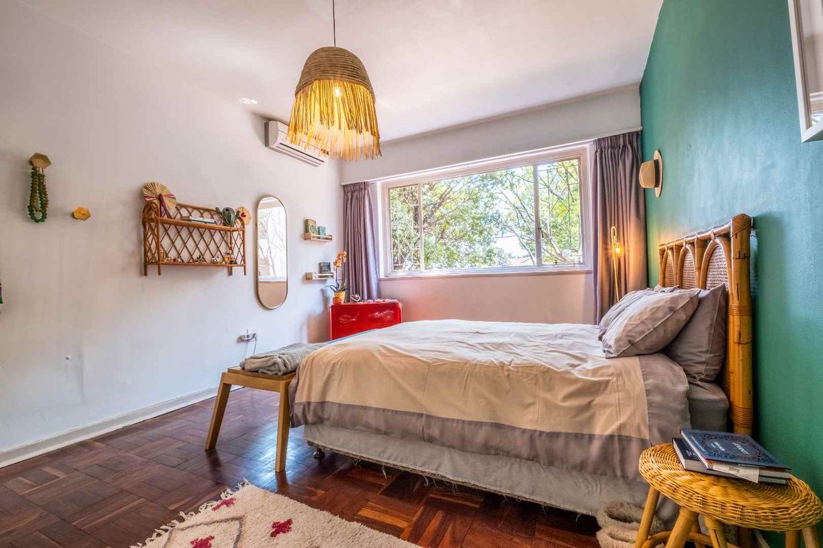 A well-lit bedroom featuring warm parquet flooring, a split-system air conditioning unit, and a large window providing natural light and garden views.