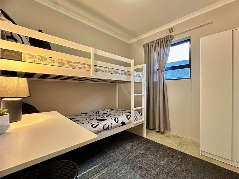 A functional bedroom featuring a built-in wardrobe, ceiling vent, and neutral finishes, providing a practical space for rest or study.