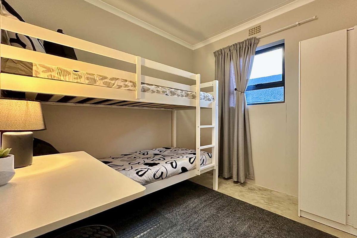 A functional bedroom featuring a built-in wardrobe, ceiling vent, and neutral finishes, providing a practical space for rest or study.
