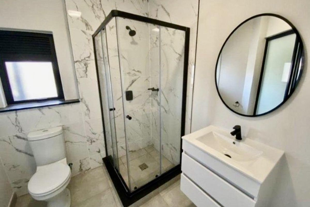 Modern bathroom featuring a glass-enclosed shower, marble-look wall tiles, a contemporary vanity with basin, and a sleek toilet.