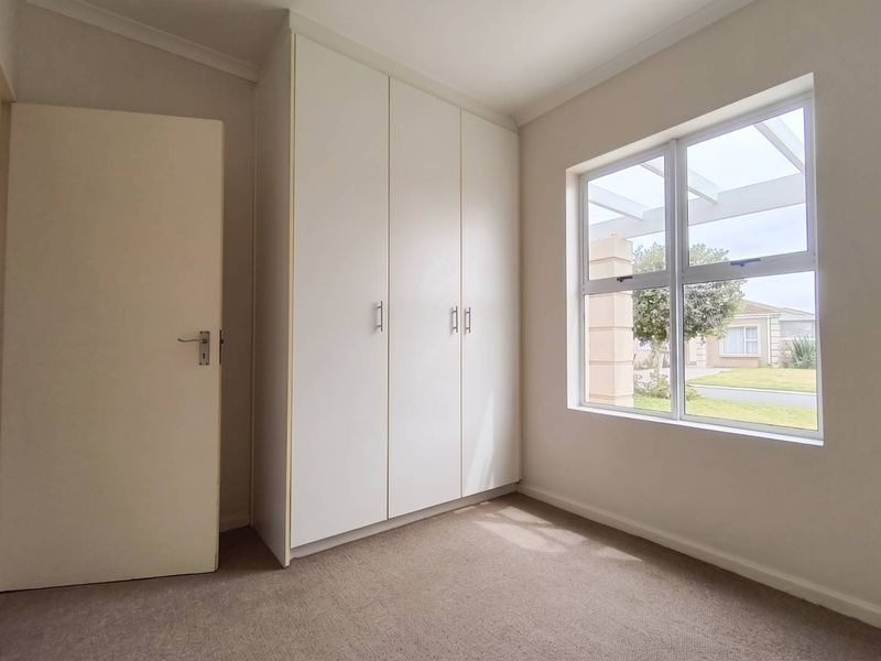 A bright and clean bedroom featuring neutral carpeting, built-in cupboards, and a large window allowing for natural light.