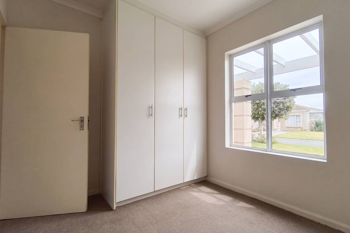 A bright and clean bedroom featuring neutral carpeting, built-in cupboards, and a large window allowing for natural light.