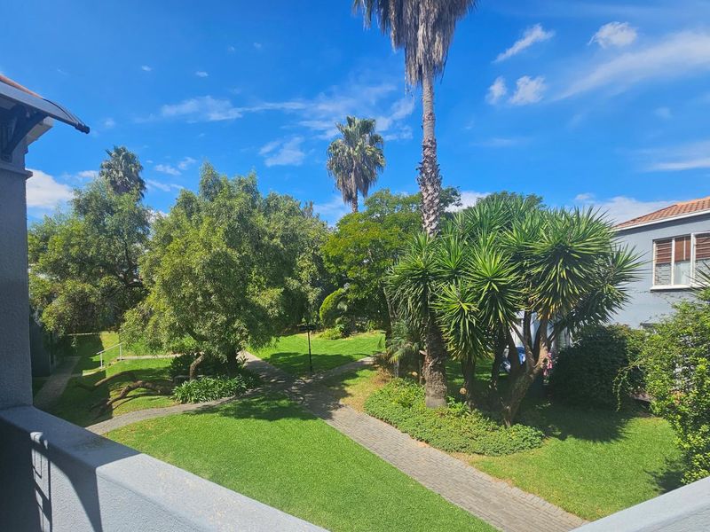 A view from an elevated balcony overlooking a well-maintained communal garden with paved walkways and mature trees.