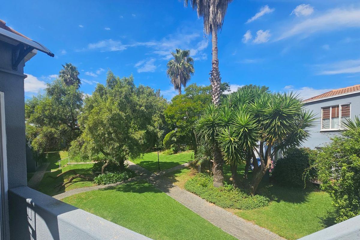 A view from an elevated balcony overlooking a well-maintained communal garden with paved walkways and mature trees.