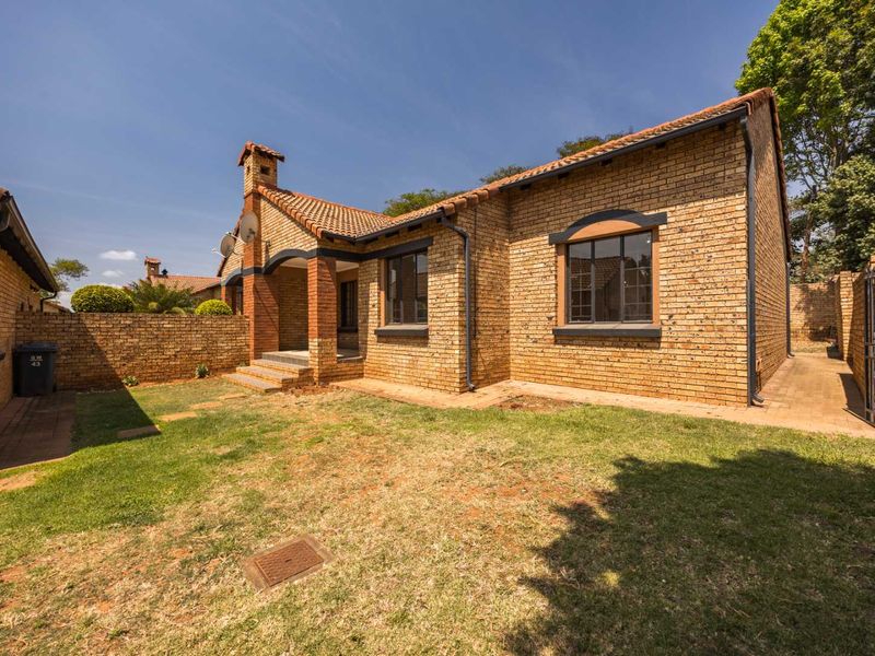 A rear view of a face brick townhouse featuring a tiled roof, chimney, and a private garden area with paved pathways.