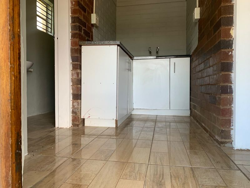 A compact kitchen area featuring exposed brick walls, tiled flooring, and basic built-in cabinetry with a countertop and sink plumbing.