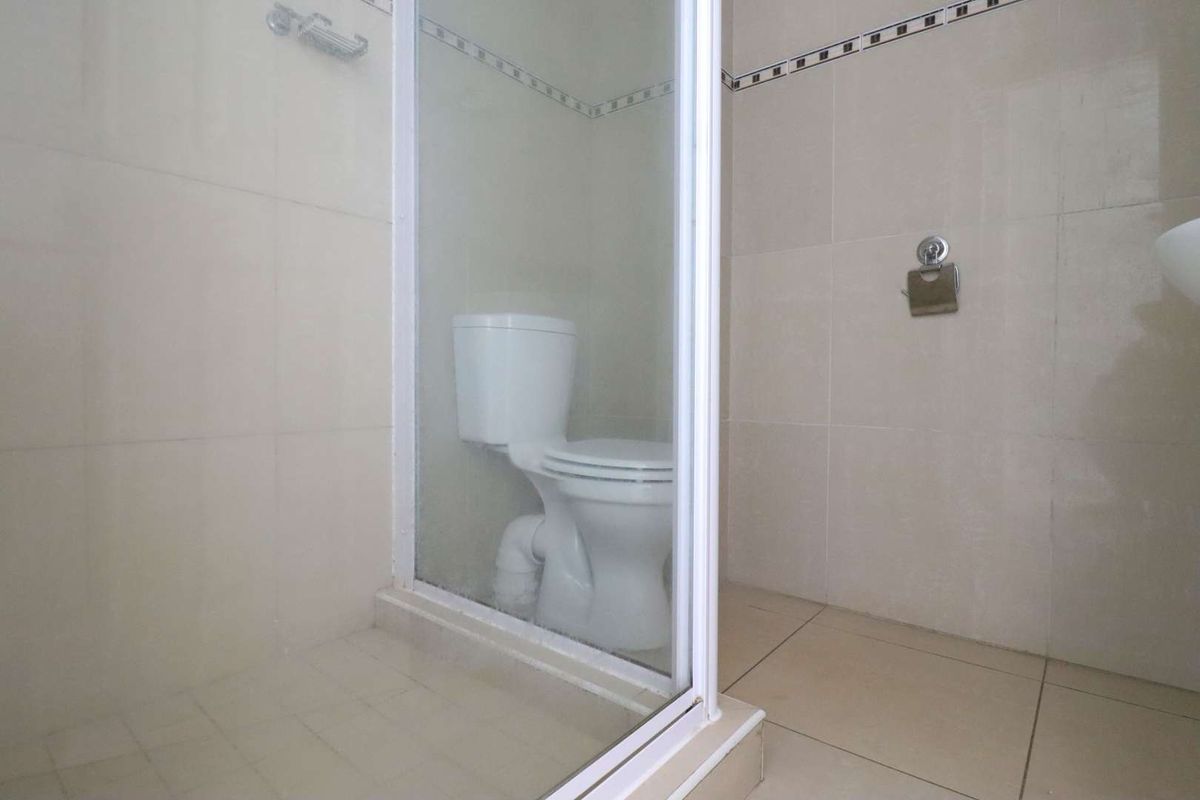 A functional bathroom featuring a glass-enclosed shower and a standard toilet with neutral wall and floor tiling.