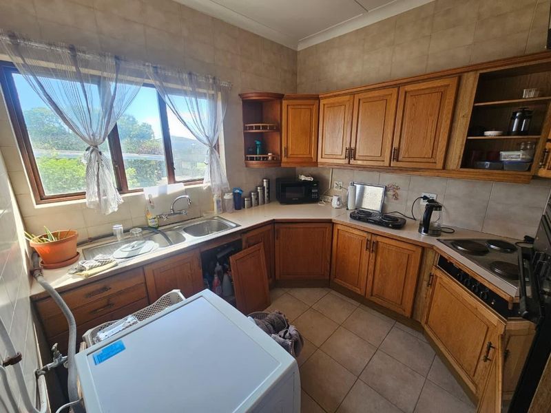 A dated kitchen featuring wooden cabinetry, tiled splashbacks, and a double basin sink, offering potential for a modern renovation.