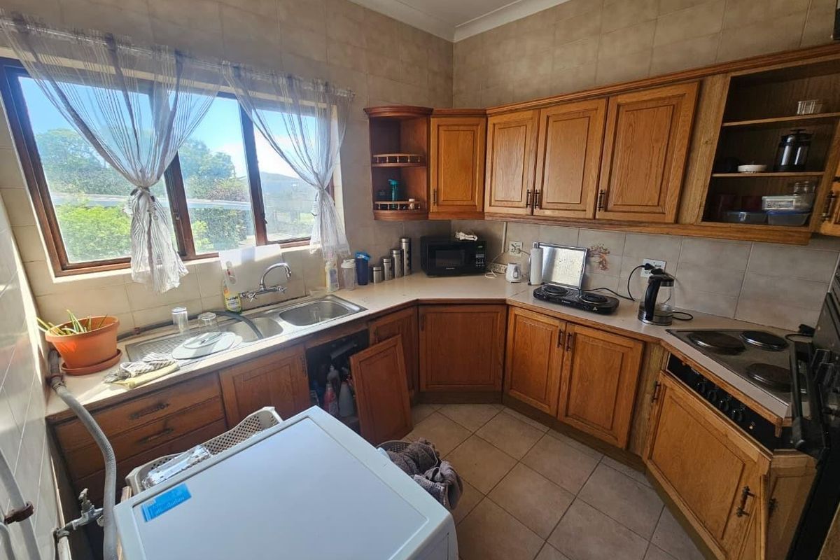 A dated kitchen featuring wooden cabinetry, tiled splashbacks, and a double basin sink, offering potential for a modern renovation.