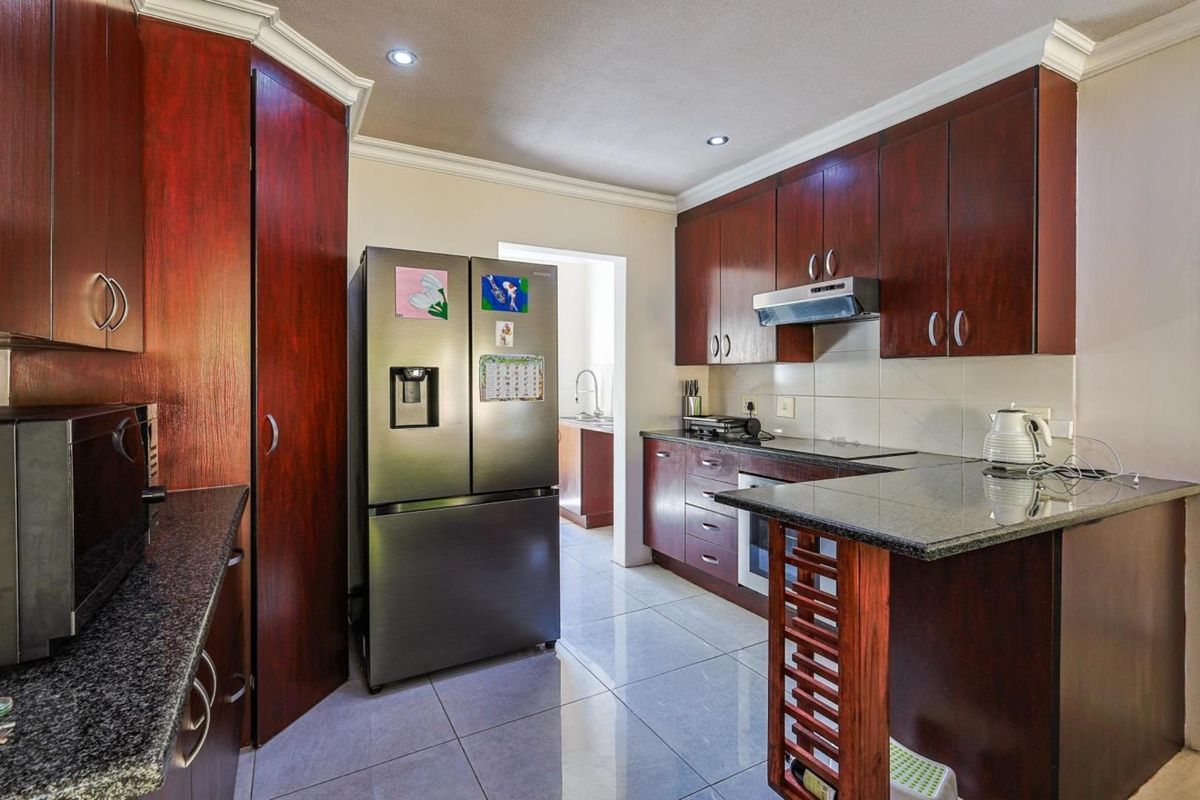 A functional kitchen featuring dark wood cabinetry, granite countertops, tiled flooring, and a built-in extractor fan, with an adjacent scullery area visible.