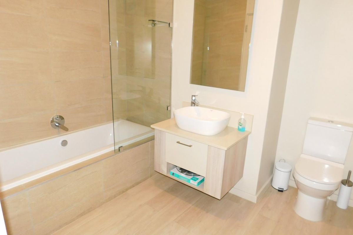 Modern bathroom featuring a floating vanity with a vessel sink, a combined bathtub and shower with a glass screen, and neutral floor tiling.