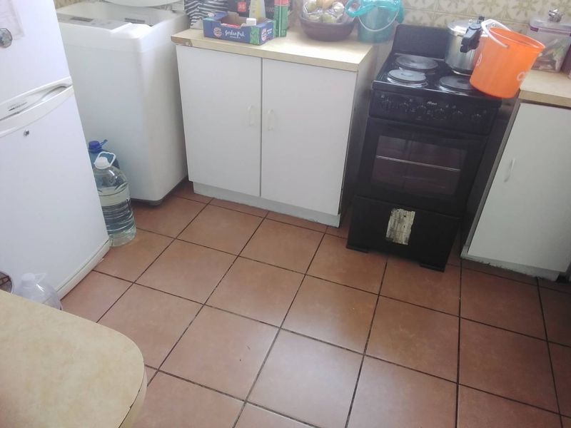 A compact kitchen area featuring tiled flooring, basic built-in cabinetry with laminate countertops, and a freestanding electric stove.