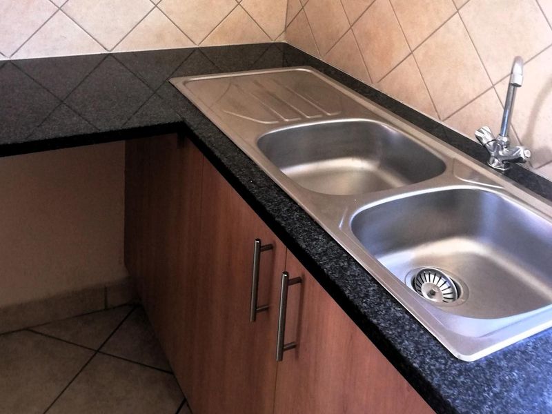 A functional kitchen corner featuring a double bowl stainless steel sink, granite countertops, and wood-finish cabinetry with a tiled backsplash.