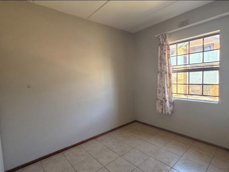 A clean, empty bedroom featuring tiled flooring, a built-in cupboard, and a window with security bars, offering a neutral canvas for personalization.