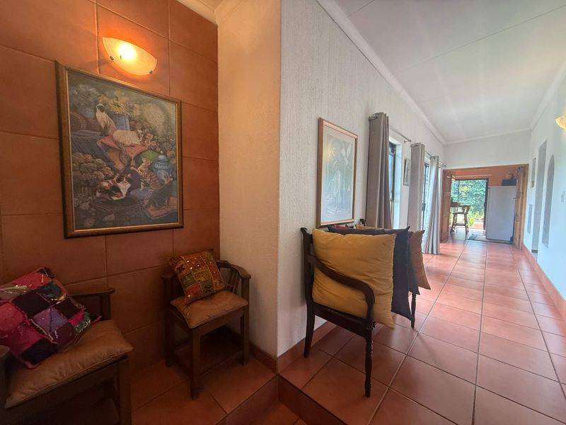A tiled hallway featuring terracotta flooring and wall-mounted lighting, leading towards an open-plan living area with access to the outdoors.