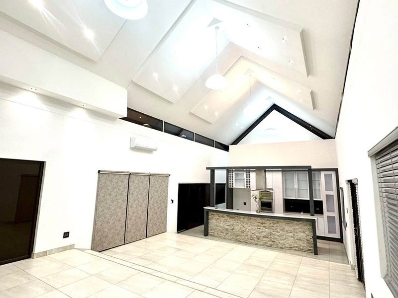 Spacious open-plan living area featuring a dramatic vaulted ceiling, tiled flooring, and a modern kitchen with a stone-clad breakfast bar and built-in cabinetry.